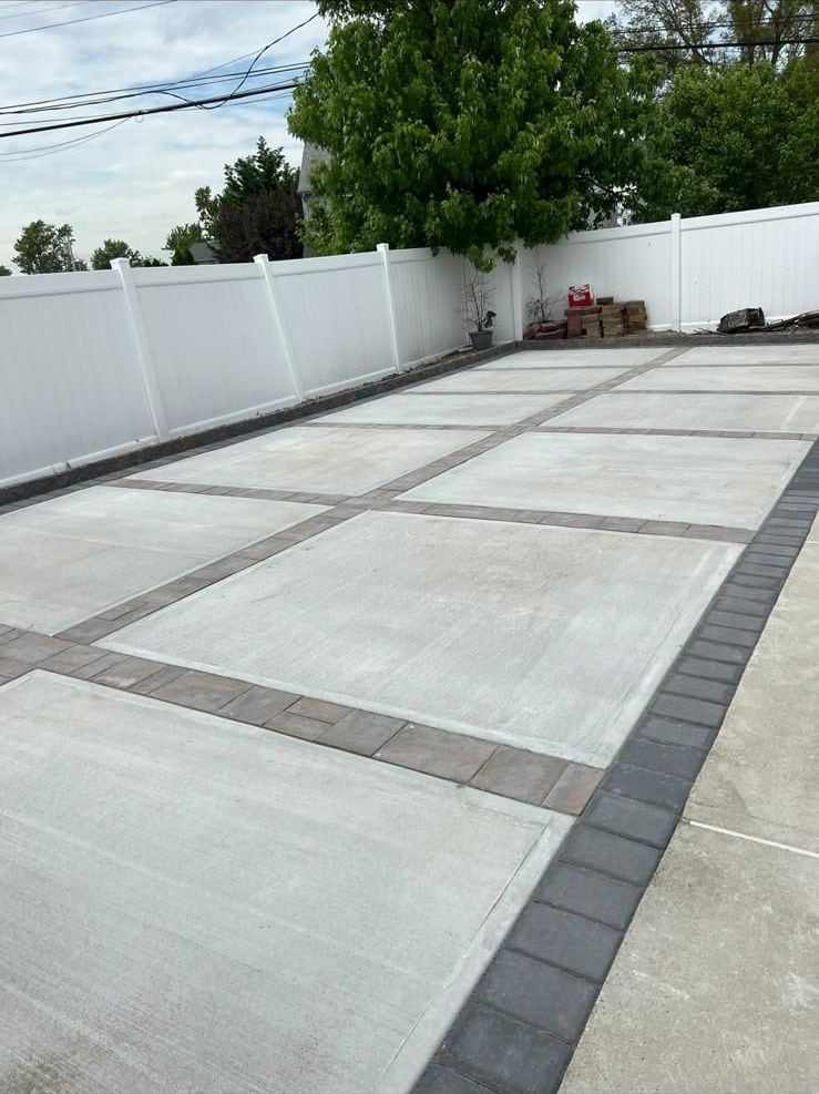 Concrete patio divided by charcoal paver bands inside a white vinyl fence in New Jersey