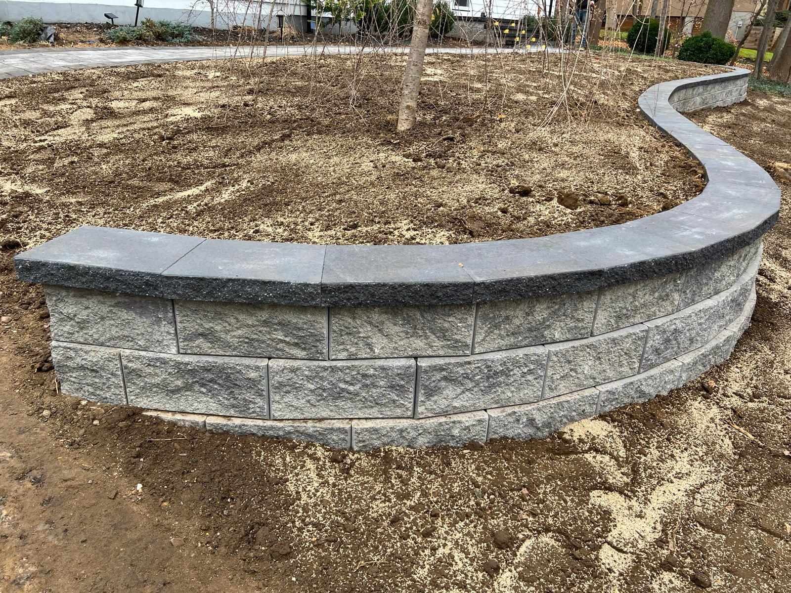 Curved segmental block retaining wall with cap stones holding a raised planting bed in New Jersey