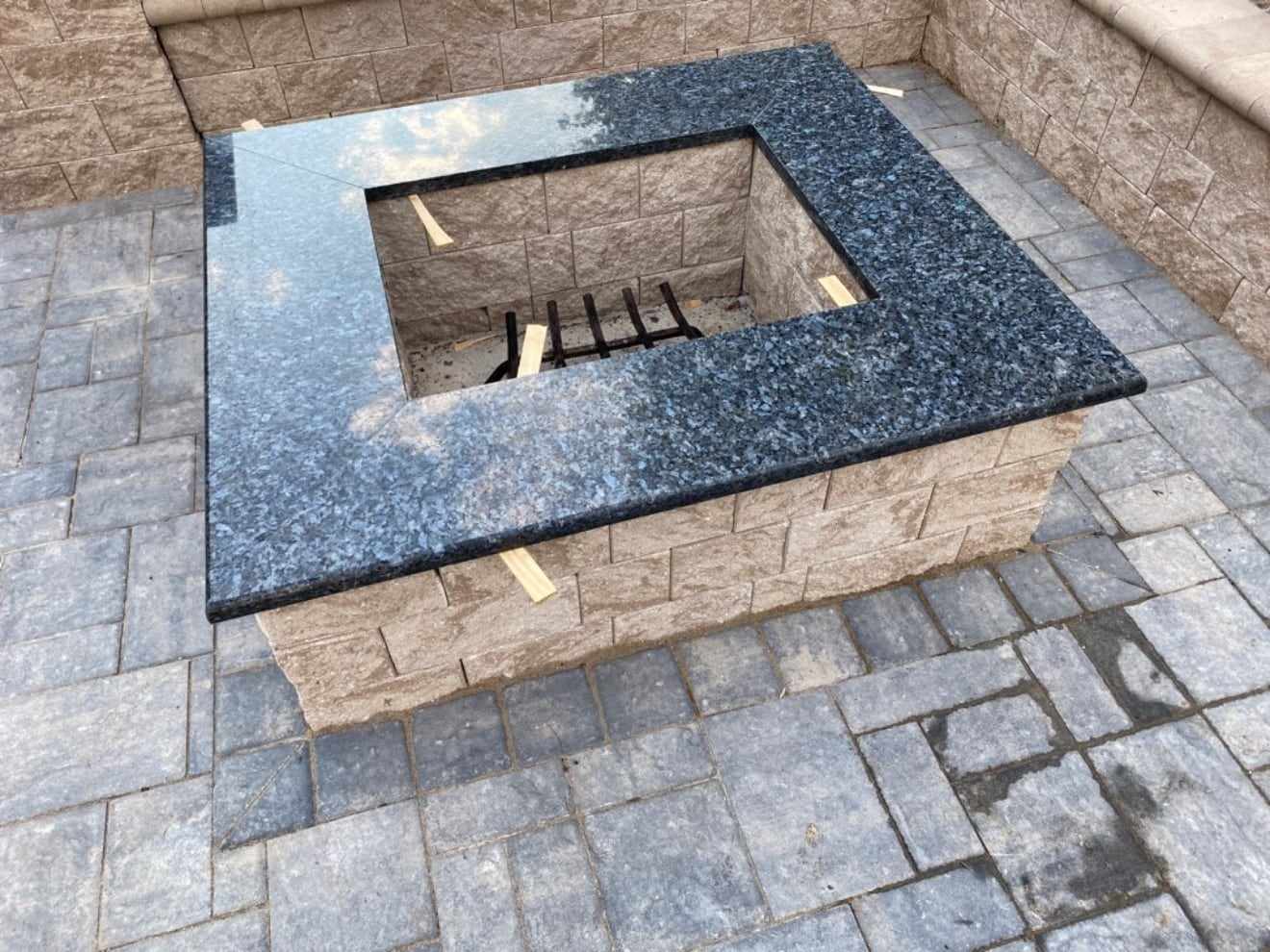 Square block fire pit with a polished granite cap on a paver patio in New Jersey