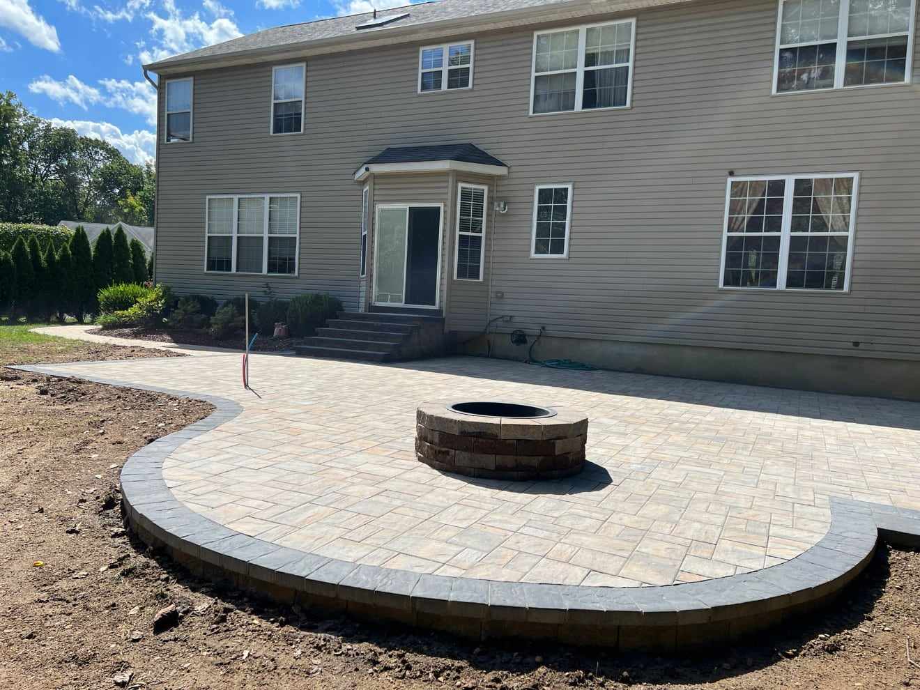 Curved paver patio with a round fire pit behind a two-story New Jersey home