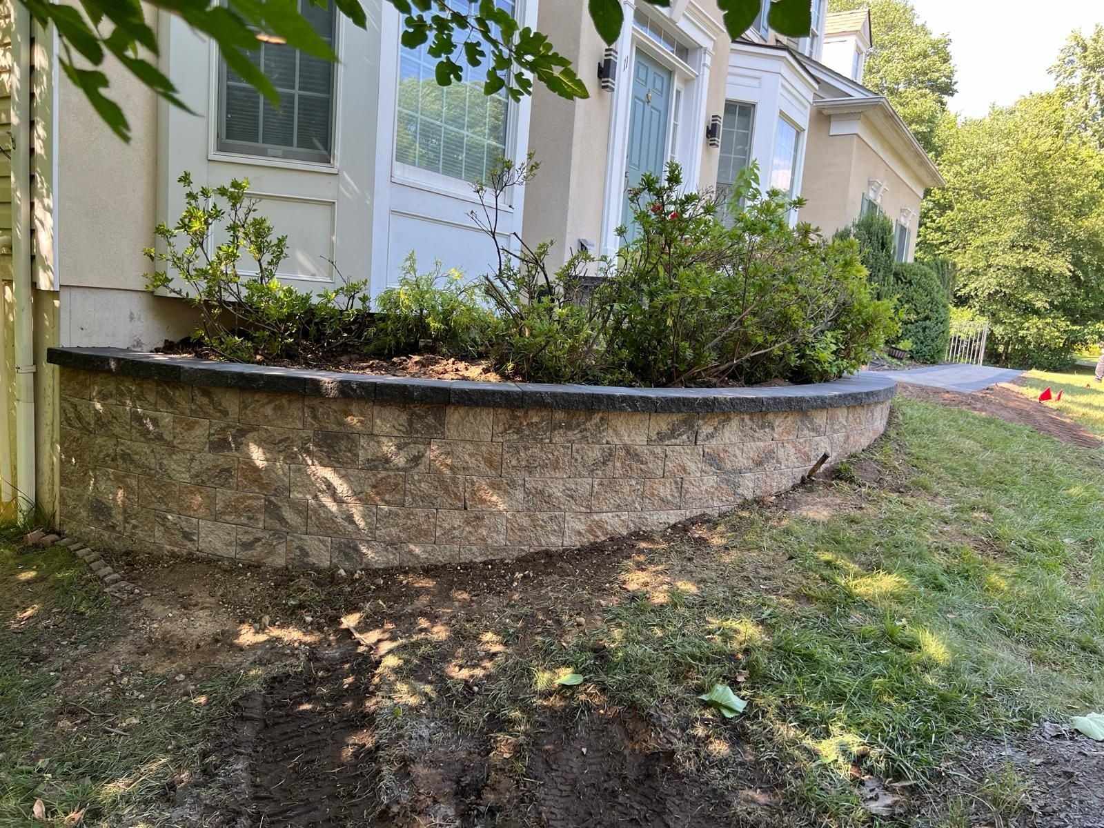 Curved stone garden wall planter along the front of a New Jersey home
