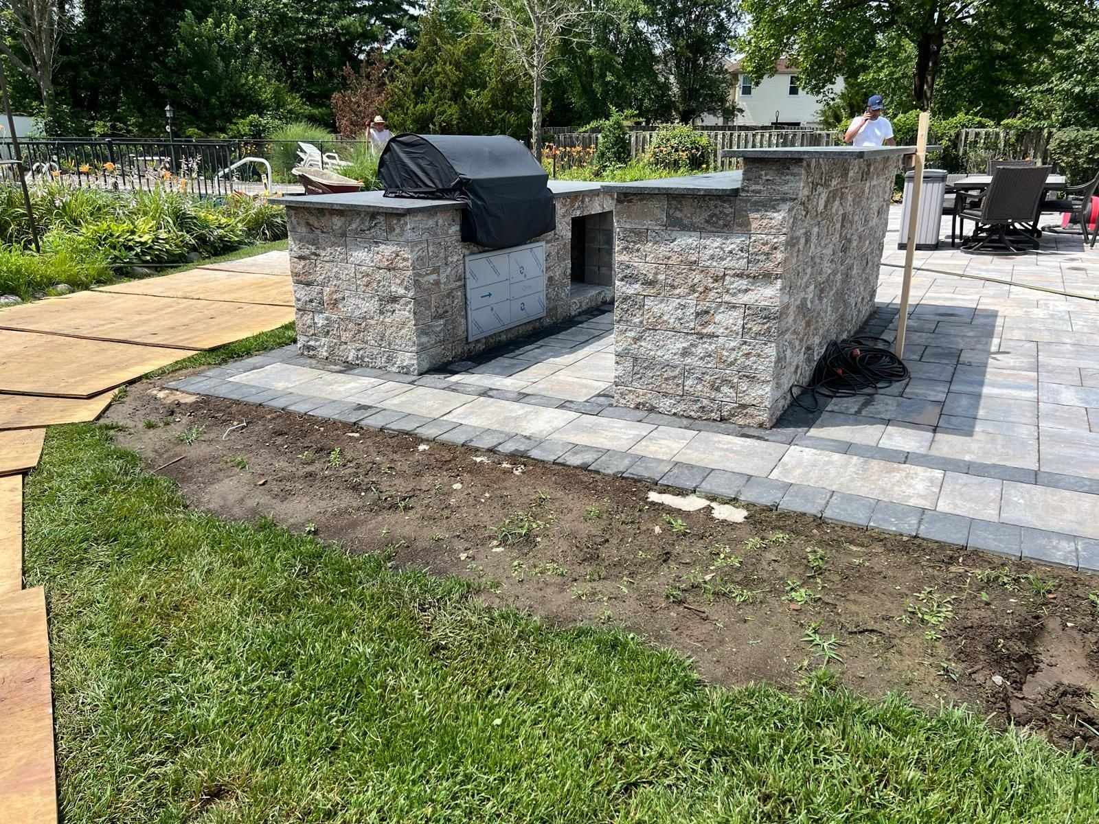 Stone-veneer outdoor kitchen grill island on a new paver patio in a New Jersey backyard