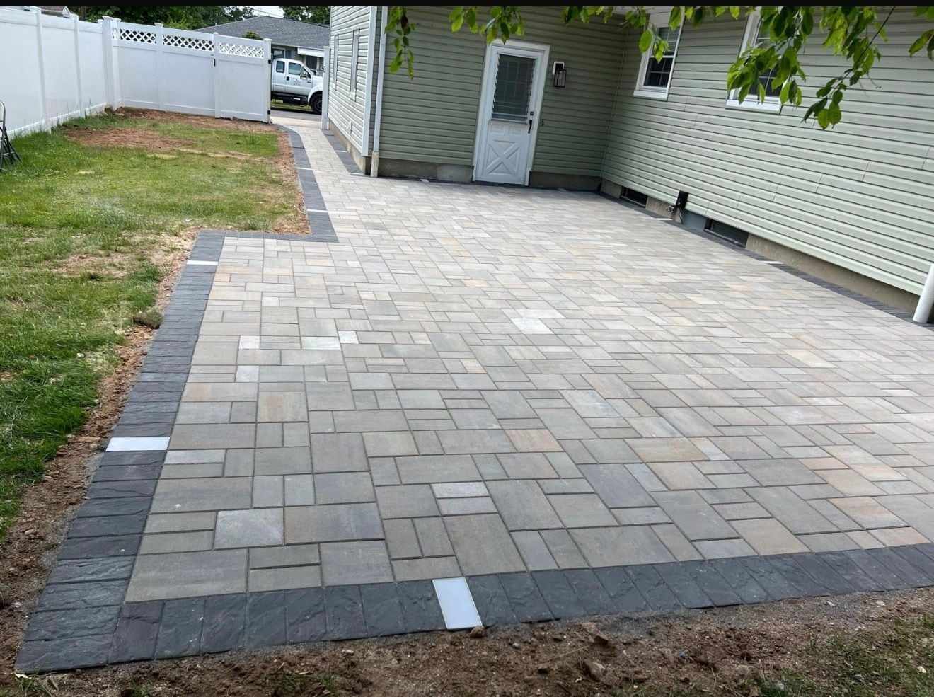 Wide backyard paver patio with a charcoal soldier-course border along a fenced New Jersey yard
