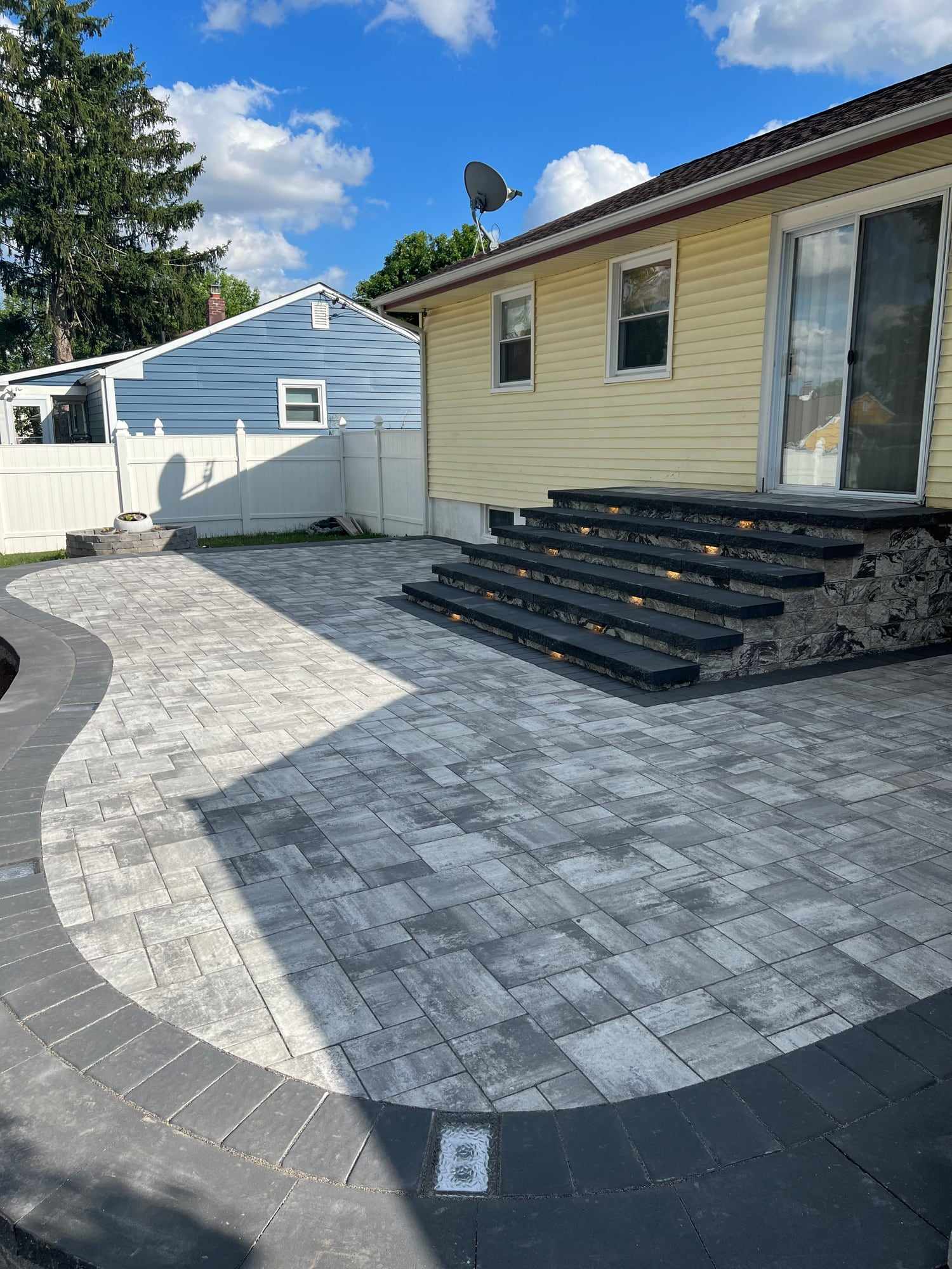 Finished curved paver patio with a wide charcoal border and paver steps to the back door in New Jersey