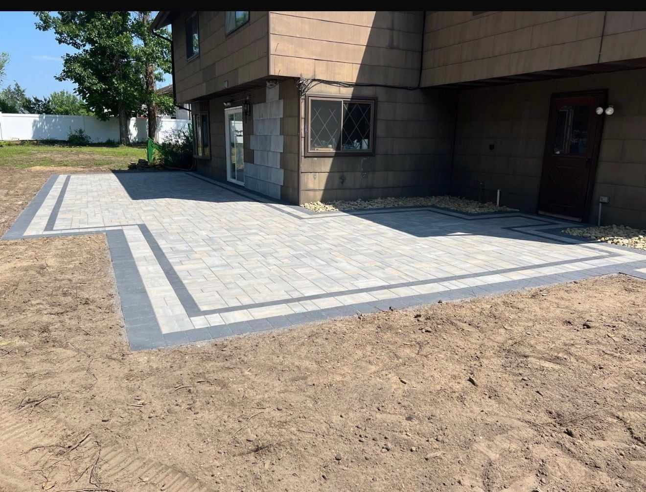L-shaped paver patio with a double charcoal border wrapping the back of a house in New Jersey