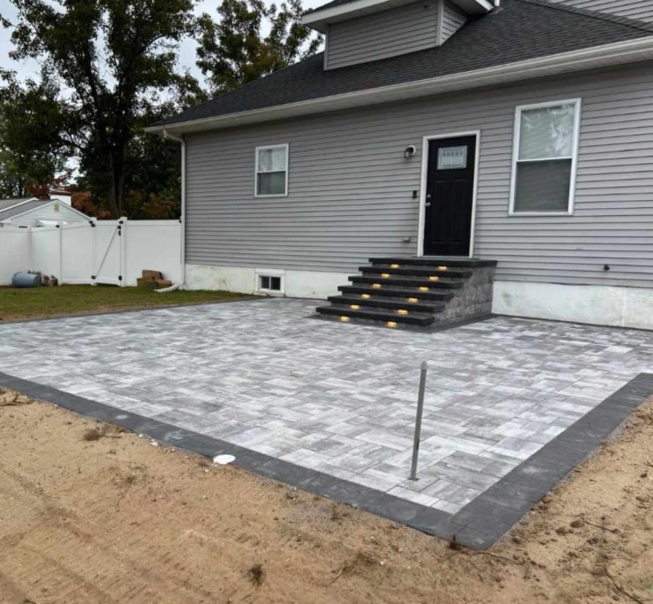 New backyard paver patio with lighted paver steps up to the rear door of a New Jersey home