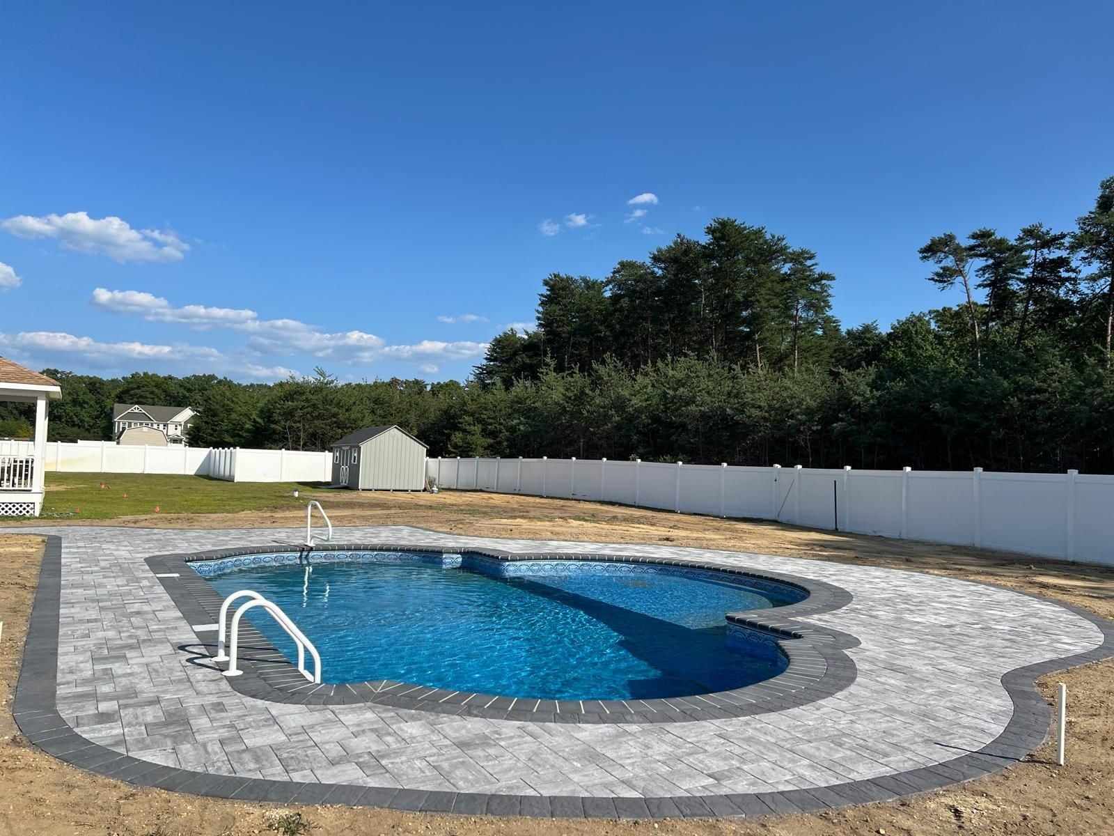 Paver pool deck with a charcoal border around a freeform in-ground pool in a New Jersey backyard