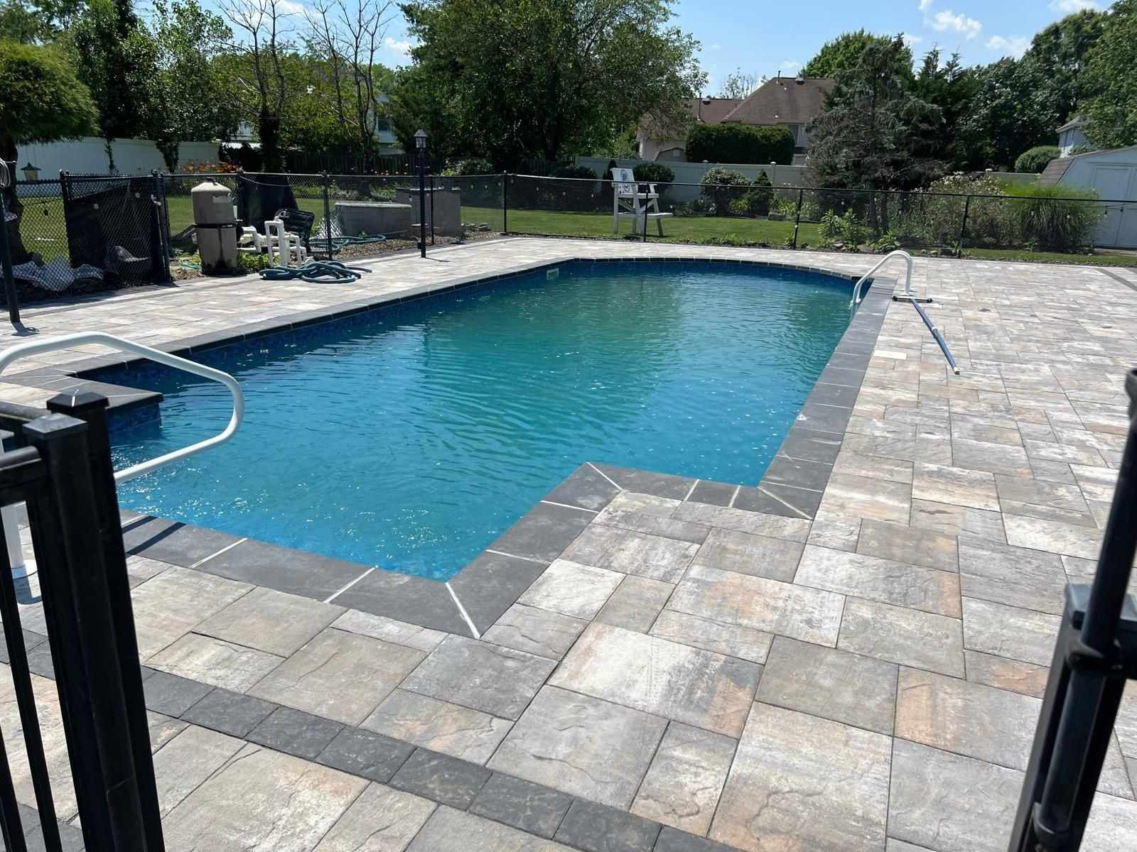 Multi-tone paver pool deck with a charcoal border inside a black pool fence in New Jersey