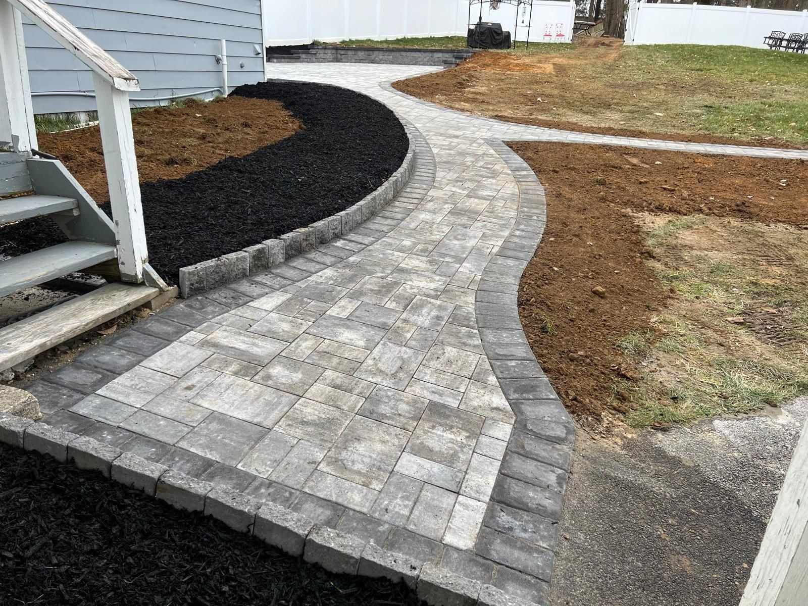 Curved paver walkway with border running from the side steps across a New Jersey yard