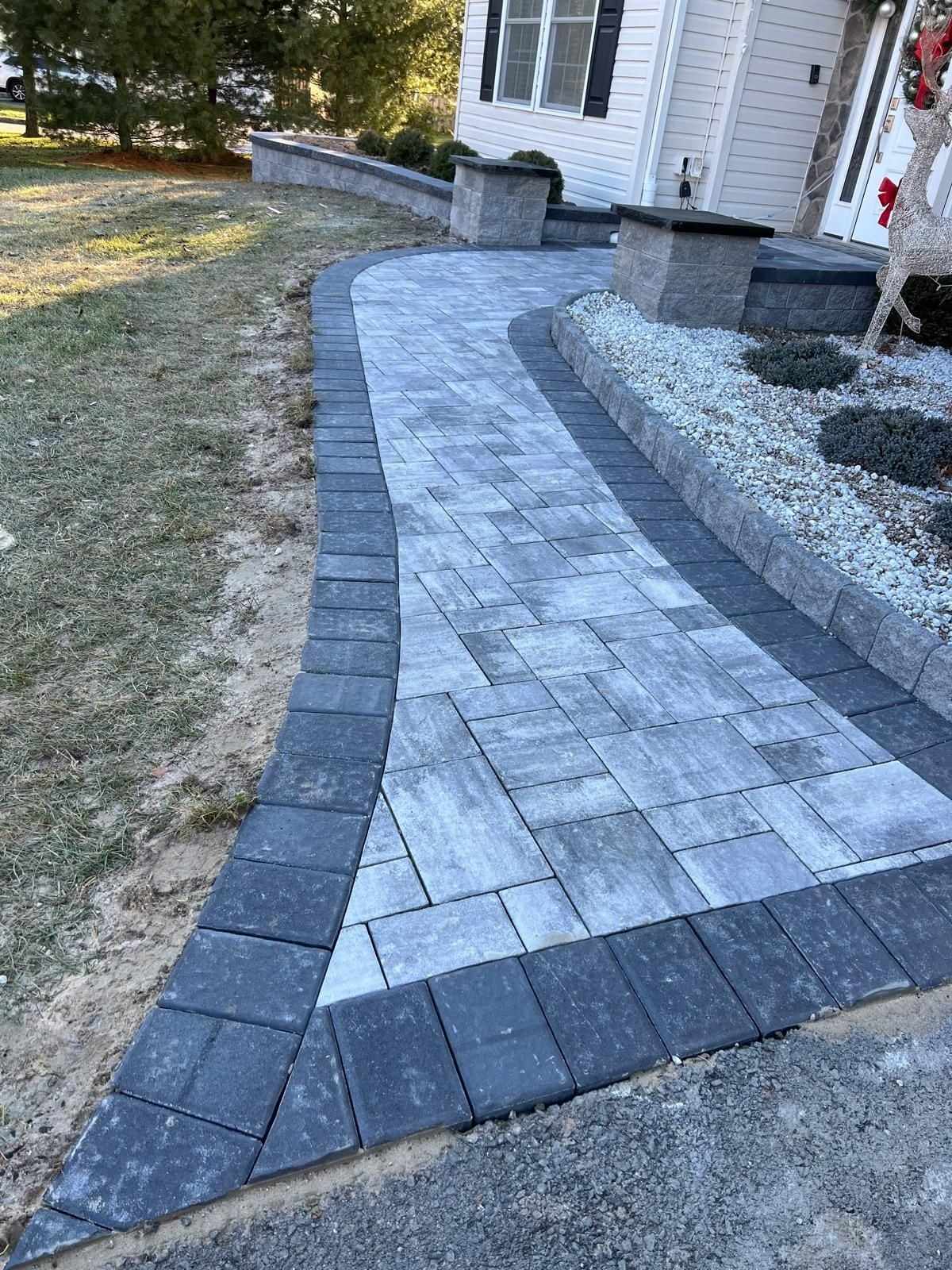 Curved gray paver walkway with charcoal border and pillars along a stone garden bed in New Jersey