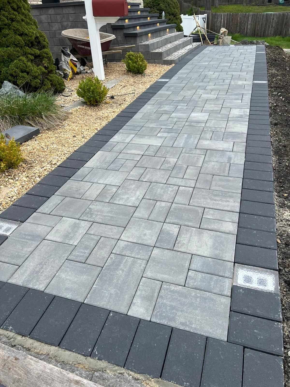 Gray paver front walkway with charcoal border and lighted steps leading to a New Jersey home