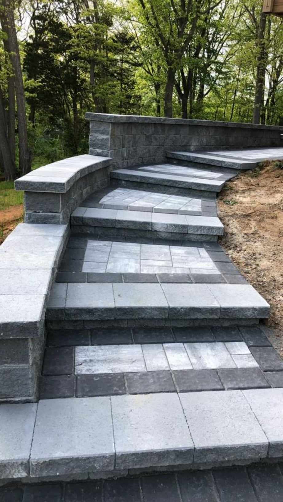 Curved paver steps climbing a wooded hillside between block retaining walls in New Jersey